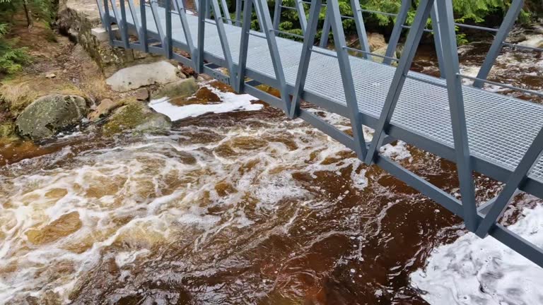 raging elements of water in a mountain river. the damaged and torn down wooden mast was washed away by the flood and crushed against the rocks. the new metal durable bridge withstands the waves of the