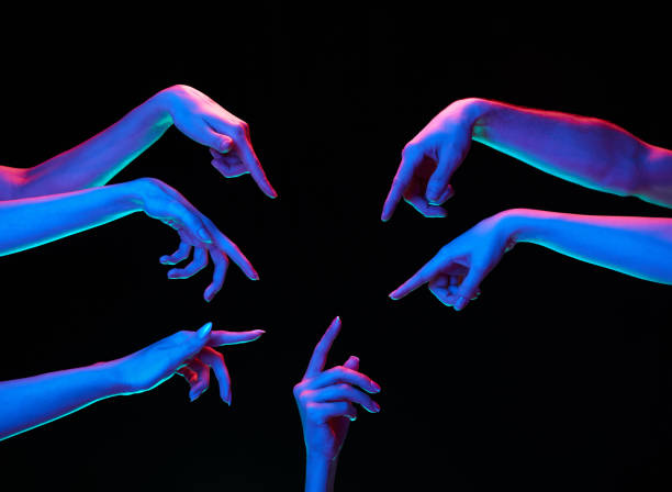 Hands in multicolored neon lighting with pointing gesture against black studio background. Opinion, self-expression.