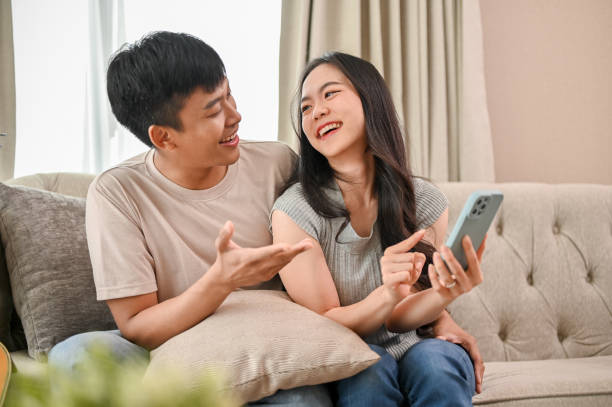 istock Happy young Asian couple enjoy talking while using a smartphone together on a sofa. 2060132600