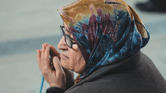 Old muslim woman praying while wearing veil with prayer beads.