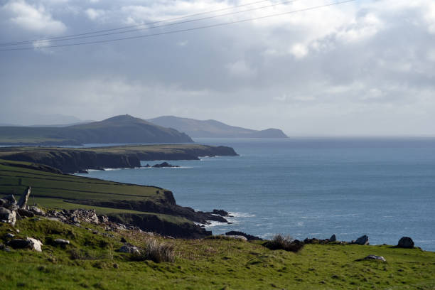 A breathtaking view of Ireland's rugged coastal cliffs, where dramatic rocky edges meet the ocean waves. The scene is accentuated by a cloudy sky, capturing the raw beauty of Ireland's untamed coastline