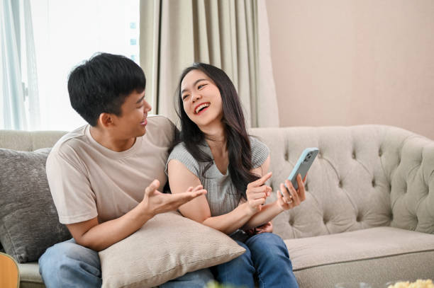 istock Happy young Asian couple enjoy talking while using a smartphone together on a sofa. 2060142510
