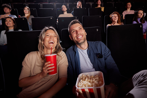 Happy couple enjoying in their drink and snack while watching a movie in theatre.