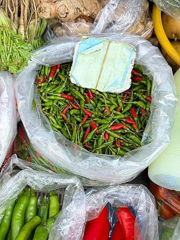 Stock photo showing close-up, elevated view of a sack of green and red chilli peppers, with green stalks, being sold by weight at an outdoor fruit and vegetable market.