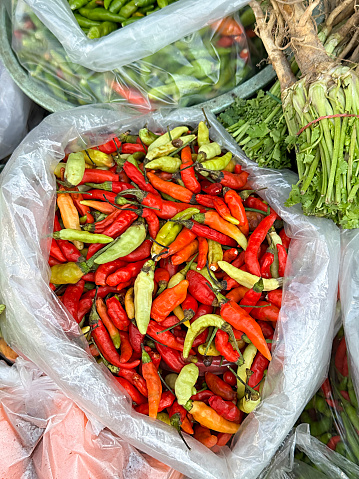 Stock photo showing close-up, elevated view of a sack of red and green chilli peppers, with green stalks, being sold by weight at an outdoor fruit and vegetable market.