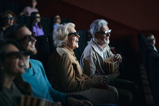 Happy mature couple with 3D glasses watching a movie in cinema. Focus is on woman.