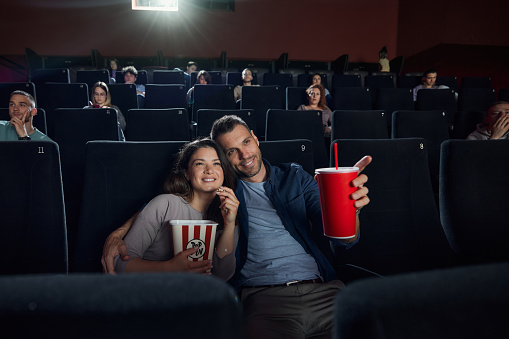 Happy couple enjoying while watching a funny movie in cinema. Man is aiming at something.