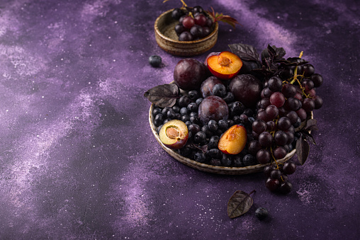 Assortment of purple fruit plum, grape, blueberry and basil on violet background