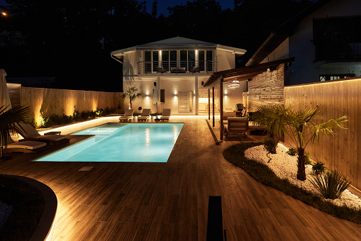 Exterior view of illuminated modern luxury house with swimming pool in foreground at night. Luxury lifestyle concept