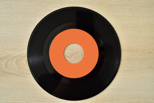 45 rpm old vinyl record on the brown wooden table. Vintage technology concept. Top view.