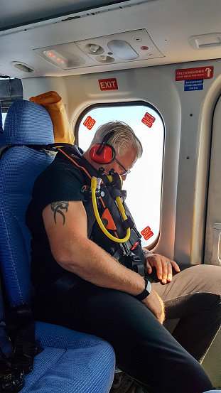 Adana, Turkey - 09/13/2019: Passenger is taking a nap inside the helicopter. Soon he will travel to offshore oil exploration rig. He wears emergency breathing apparatus on top of his daily clothes.