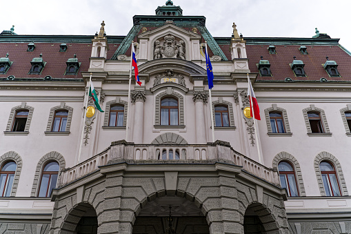 Facade of university building at the old town of City of Ljubljana with flags on a cloudy summer day. Photo taken August 9th, 2023, Ljubljana, Slovenia.