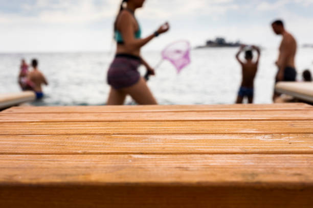 Empty wooden table at the beach with people swimming at sea in background. Empty, blank space for montage