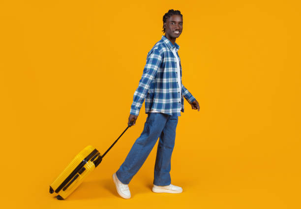 istock Smiling young black man casually walking with yellow suitcase on orange background 2060224187