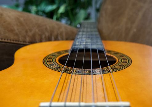 Perspective view of an acoustic guitar on a leather armchair.