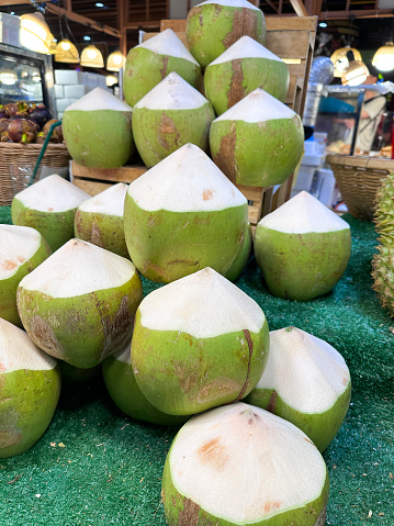 Stock photo showing close-up view of fresh fruit produce, selling immature coconuts displayed at market on a street food market stall covered with APAC artificial grass matting.