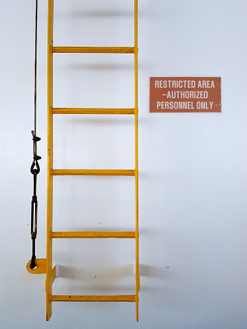 Yellow ladder on a white wall with a warning sign that says that it is forbidden to climb