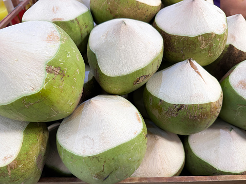 Stock photo showing close-up, elevated view of fresh fruit produce, immature coconuts displayed at market on a street food market stall.