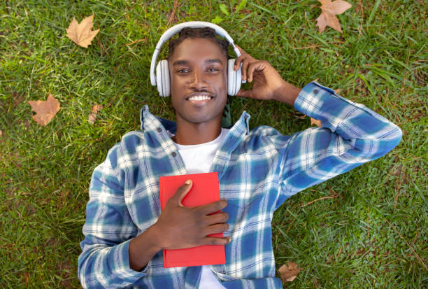 istock black guy with headphones and book lying outdoors, top view 2060249233