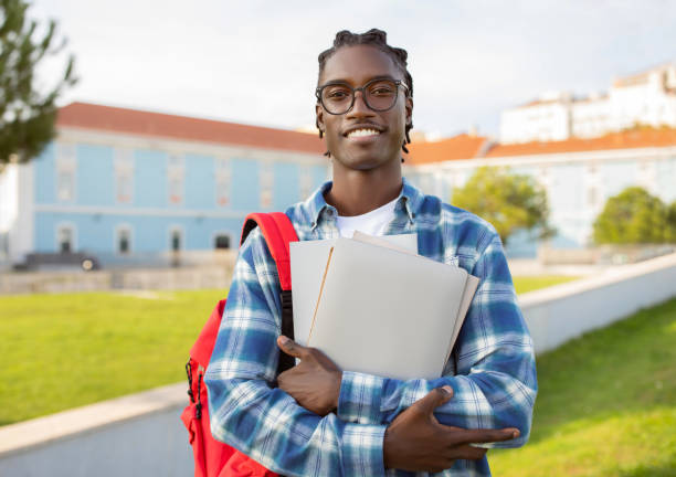 istock black student guy stands with laptop, backpack and books outside 2060249271