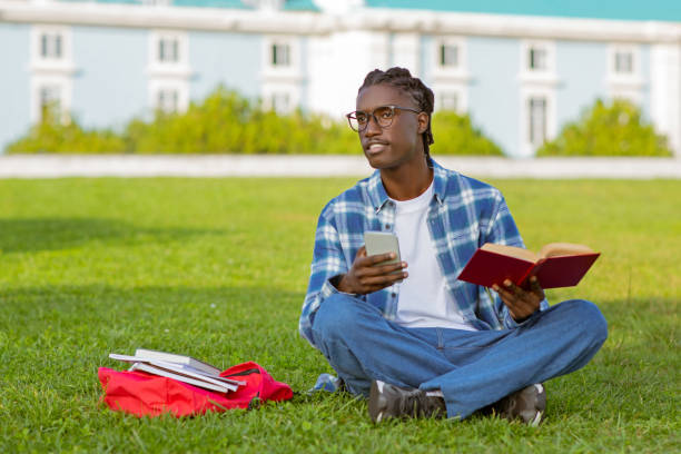 istock black student guy holding mobile phone and book learning outdoor 2060249958
