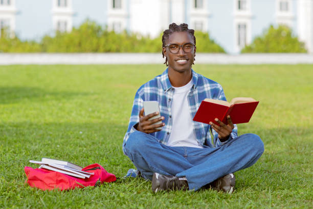 istock Cheerful African American student guy holding cellphone and book outside 2060249960