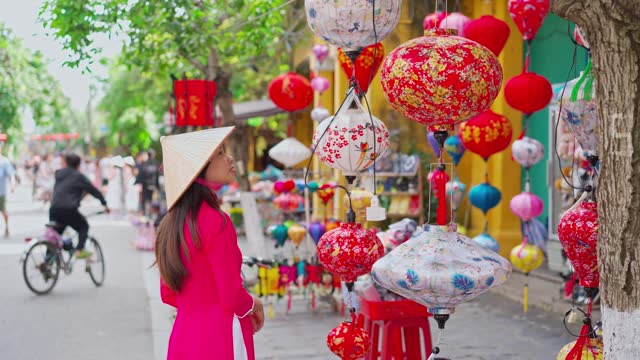 Young female tourist in Vietnamese traditional dress looking at a souvenir shop in Hoi An Ancient town