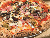 Full fame image of sliced ham and mushroom pizza with black olives on wooden table, elevated view, focus on foreground