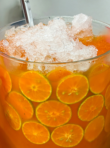 Stock photo showing close-up view of a glass jug containing orange juice with orange citrus fruit slices, ice cubes and crushed ice slushy covered in condensation showing the cold temperature of the beverage.