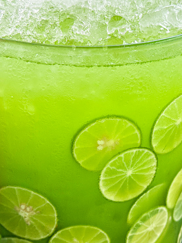 Stock photo showing close-up view of a glass jug containing lemon and lime juice with lime citrus fruit slices, ice cubes and crushed ice slushy covered in condensation showing the cold temperature of the beverage.