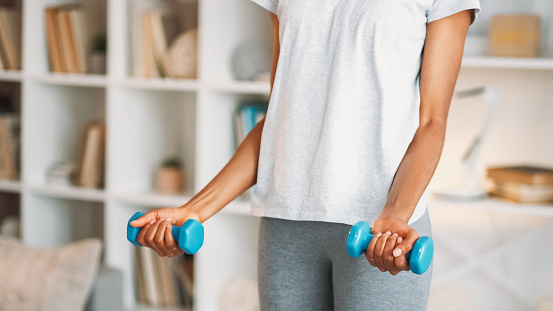 Dumbbells training. Home gym. Athletic fit healthy woman in activewear enjoying weights muscle physical aerobics workout indoors in living room.