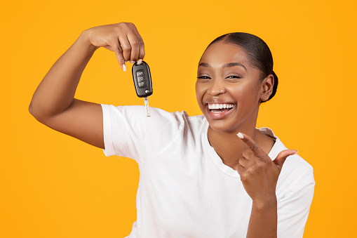 New Car. Excited Black Woman Showing Key In Excitement Celebrating Buying New Auto On Yellow Studio Background, Smiling To Camera. Dreams Come True, Own Vehicle Purchase Concept