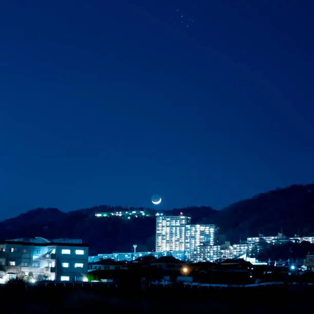 The moon setting over the mountains beyond the buildings