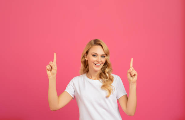istock blonde woman pointing fingers upwards with both hands on pink 2060287272