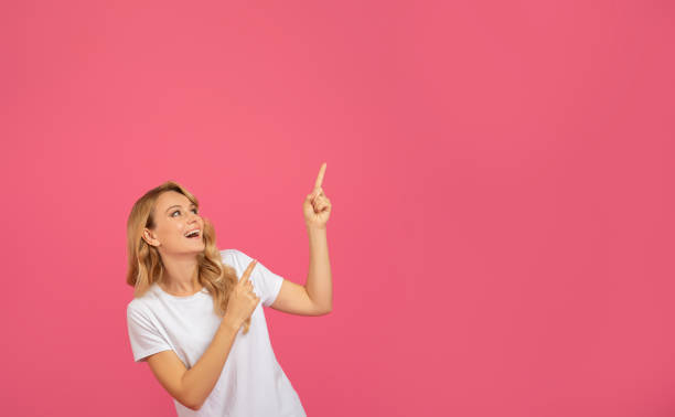 istock Excited Blonde Woman Pointing Fingers Upward At Copy Space, Studio 2060287787