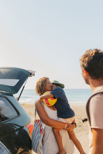 Photo of an adventurous family with two young boys, on a summer road-trip with a family car, who's found a perfect local beach for a hot summer day