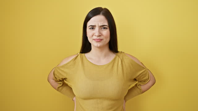 Furious young hispanic woman channels her anger, screaming and shouting expressively. beautiful brunette, shrouded in yellow isolated background, exudes aggression through her unhappily frustrated face.