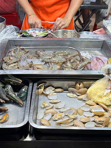 Stock photo showing close-up, elevated view of trays of freshly caught piles of shellfish, clams, shrimp and green lipped mussels being prepared for eating before being sold at the fish market fishmongers.