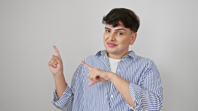 Cheerful young man wearing stripes shirt, confidently standing and pointing to the side with both hands against isolated white background. looking straight at the camera with a big happy smile.