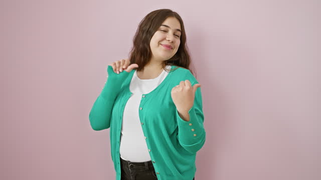 Cheery young hispanic lady confidently thumbs up, pointing gracefully behind over isolated pink backdrop, beaming with accomplishment