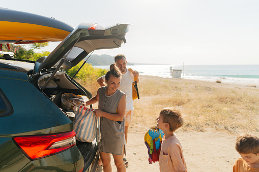 Photo of an adventurous family with two young boys, on a summer road-trip with a family car,  found a perfect local beach to spend a hot summer day