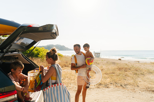 Photo of an adventurous family with two young boys, on a summer road-trip with a family car,  found a perfect local beach to spend a hot summer day