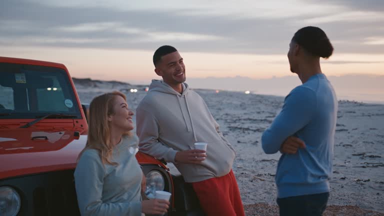 Young Woman Standing By Car With Hot Drink At Beach Watching Sunrise