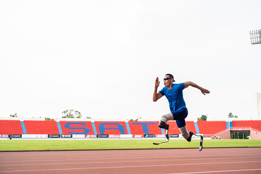 Asian para-athletes disabled with prosthetic blades running at stadium. Attractive amputee male runner exercise and practicing workout for Paralympics competition regardless of physical limitations.