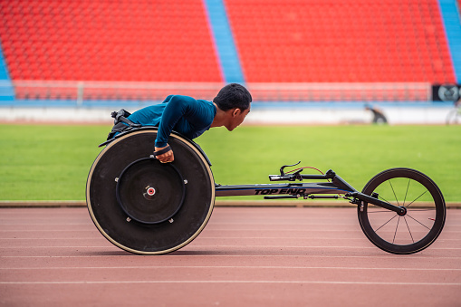 Asian young man para-athletes disabled practice handcycling in stadium. Attractive amputee male runner exercise and practicing workout for Paralympics competition regardless of physical limitations.