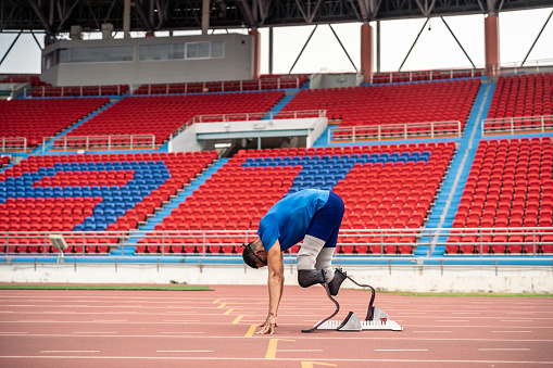 Asian para-athletes disabled with prosthetic blades running at stadium. Attractive amputee male runner exercise and practicing workout for Paralympics competition regardless of physical limitations