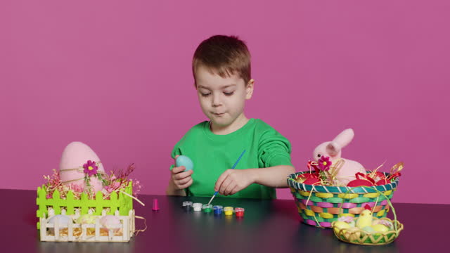 Little cheerful boy crafting handmade easter decorations by painting