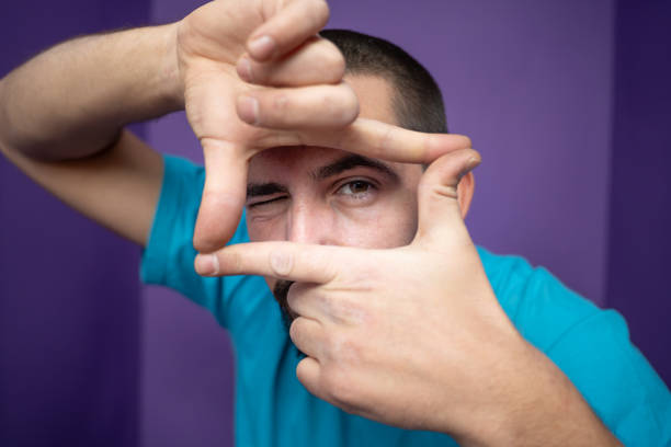 Young handsome man doing frame using hands palms and fingers, over purple background Young handsome man doing frame using hands palms and fingers, over purple background. High quality photo hand cropping photos stock pictures, royalty-free photos & images