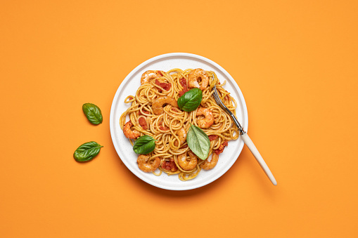 Shrimp marinara sauce pasta in plate on orange background with copy space