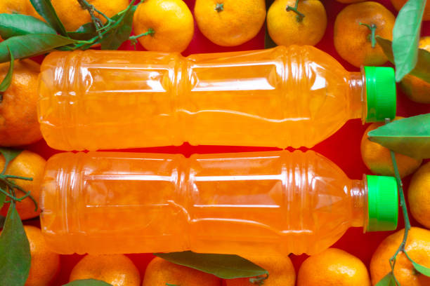 Vibrant and refreshing orange juice in plastic bottles, accompanied by fresh whole oranges as decoration, set against a striking red background. Perfect for showcasing a healthy beverage or fruit-related product. This image highlights the natural appeal of citrus fruits and is ideal for use in food and beverage marketing, product packaging, or health-related promotions.